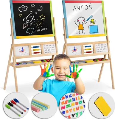A young child with painted hands smiles in front of a double-sided easel with educational elements.