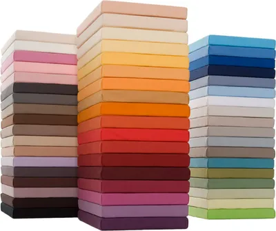 Three stacks of colorful fitted sheets are arranged in a studio setting against a white background.
