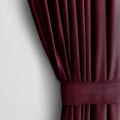 A close-up view of a burgundy velvet curtain with pleats and a tie-back.