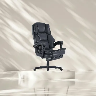 A black executive chair with a footrest is displayed on a white pedestal against a light gray background with abstract shadows.