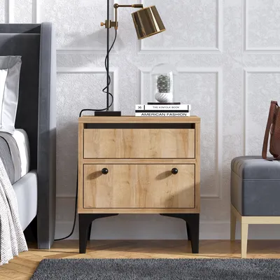 A bedside table with drawers next to a bed, with a lamp and books on top.