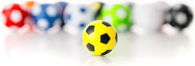 A single yellow and black soccer ball is in focus in the foreground, with a line of other colorful soccer balls blurred in the background.