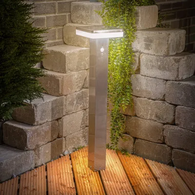 A solar-powered garden light is shown in an outdoor setting, surrounded by stone steps and wooden decking.