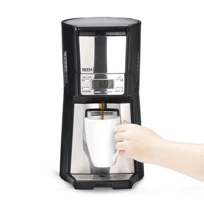 A coffee maker is brewing coffee into a white mug, with a hand holding the mug.
