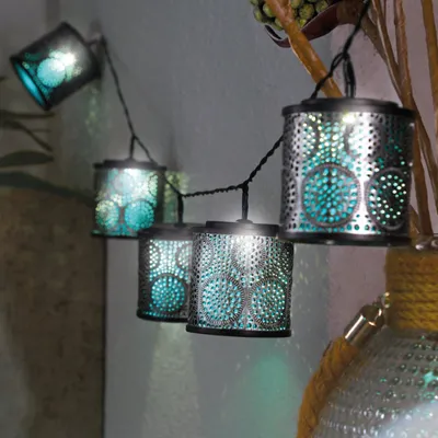 A string of solar lanterns with a Moroccan-inspired design, illuminated and casting patterns of light on a wall.