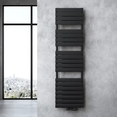 A black radiator is mounted on a concrete wall next to a large window with a view of a snowy landscape.