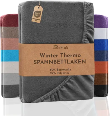 A folded grey fleece fitted sheet is displayed prominently, with other colored sheets visible behind it. A brown paper band wraps around the main sheet, featuring product information.