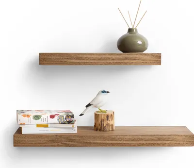 Two wooden shelves mounted on a white wall, decorated with books, a decorative bird, and a vase with reeds.