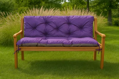 A purple and gray tufted cushion on a wooden garden bench, set in a grassy yard with tall ornamental grasses and trees in the background.