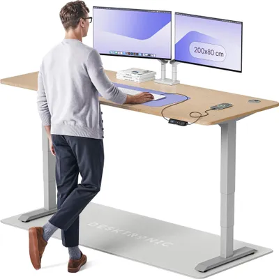 A man is standing at a height-adjustable desk with two monitors.