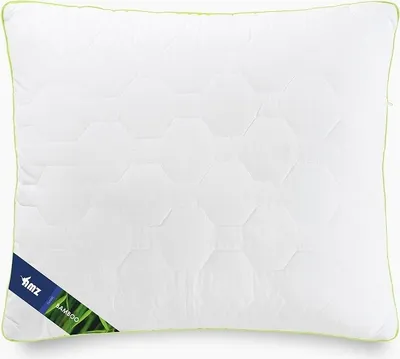 A white pillow with a hexagonal pattern and a green trim. A blue label with white text and a green leaf design is attached to the bottom left corner.
