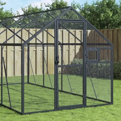 A greenhouse structure in a grassy yard with a wooden fence in the background.