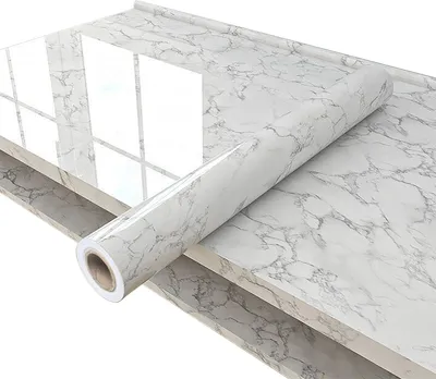 A roll of marble-patterned wallpaper is placed on a countertop, with a section already applied to the surface.