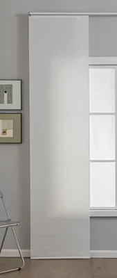 A white sliding curtain panel is shown covering a window in a room with a gray wall and a wooden floor. Two framed pictures hang on the wall to the left of the curtain, and a metal chair is partially visible in the bottom left corner.