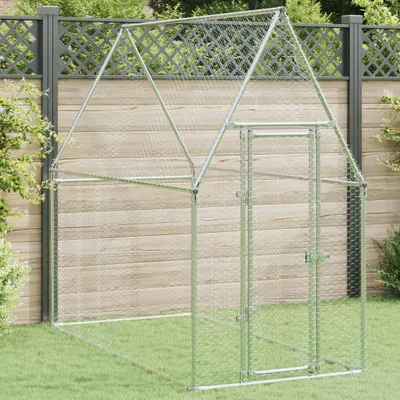A silver chicken coop is set up on a grassy lawn in front of a wooden fence.