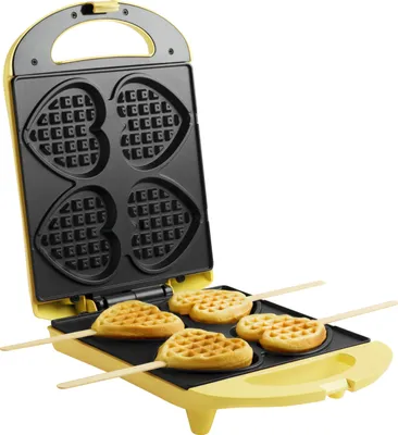 A yellow waffle maker with heart-shaped molds and waffles on sticks.