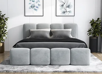 A modern bedroom setting with a gray upholstered bed, matching ottomans, and abstract art on the wall.