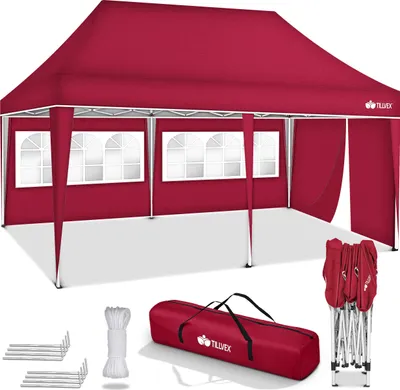 A red pop-up tent with windows and side walls, along with its accessories, laid out on a white surface.