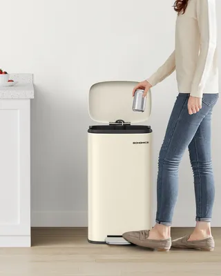 A person is putting a can into a cream-colored kitchen trash can.