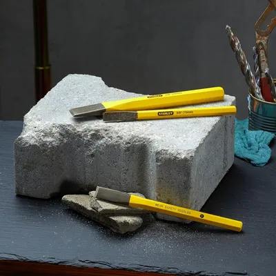 Three yellow chisels are placed on a large gray stone block, with smaller stone fragments in the foreground.