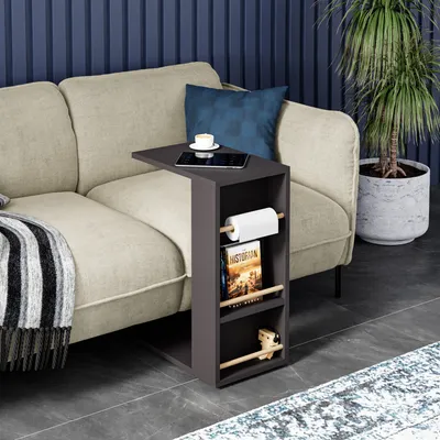 A side table is placed next to a sofa, holding a tablet, a cup of coffee, a roll of paper towels, and books.