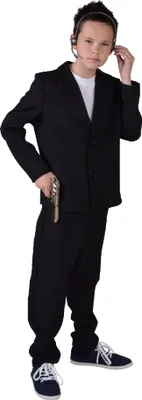 A young boy dressed as a bodyguard, wearing a suit and headset, holding a toy gun.