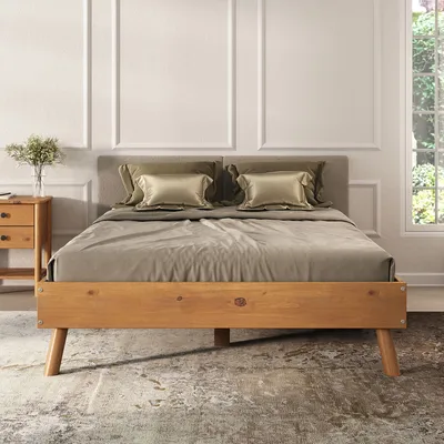 A bed with wooden frame and gray headboard, dressed with bedding and pillows, in a room with decorative wall molding and a window with greenery outside.