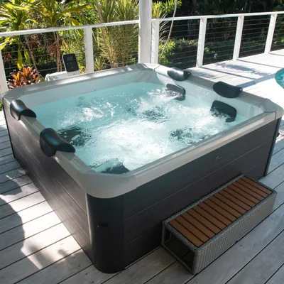 A hot tub filled with bubbling water on a wooden deck, surrounded by lush greenery and a white railing.