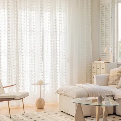 A bright and airy living room with white sheer curtains, a sofa, and a chair.