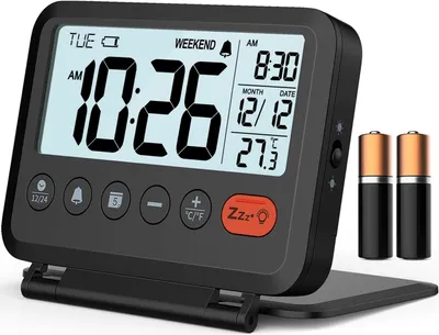 A digital alarm clock is shown in an open, folded position, with two batteries placed next to it.