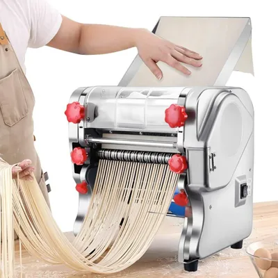 A person is using a stainless steel noodle maker to produce fresh noodles.