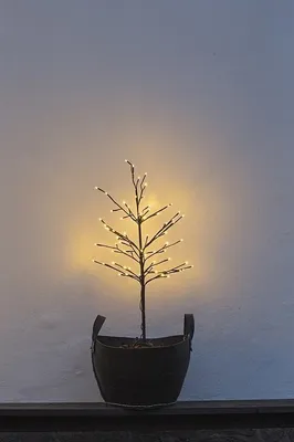 A small LED tree in a pot is placed on a dark surface against a light-colored wall.