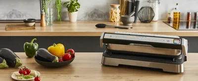 A kitchen counter with a grill and fresh vegetables.
