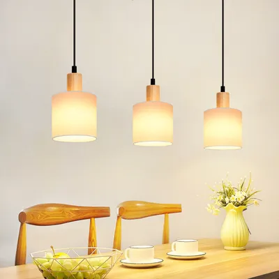 Three pendant lights hanging over a dining table with chairs, fruit bowl, and cups.