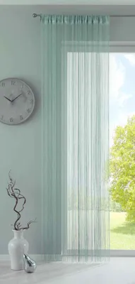 A mint-colored string curtain hangs in front of a window with a view of trees and sky. A clock is on the wall to the left, and a vase with branches and a decorative object are on the floor.