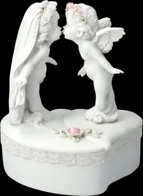 A white ceramic music box shaped like a heart, decorated with figures of a bride and an angel kissing.