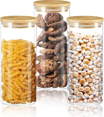 Three glass storage jars with bamboo lids, filled with pasta, dried mushrooms, and small white beans.