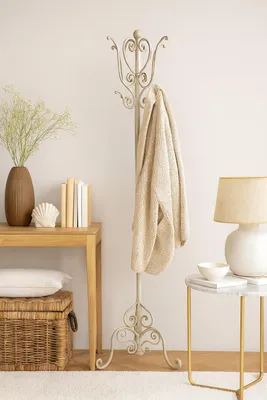 A coat rack with a sweater draped over it, next to a table with books and a lamp.