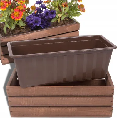 A brown plastic planter insert sits inside a brown wooden crate. Another planter with flowers is visible in the background.