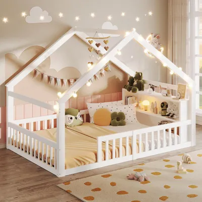 A child's house-shaped bed decorated with fairy lights and stuffed animals.