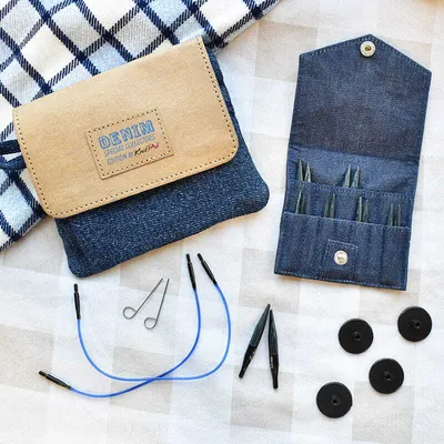 A flat lay of knitting needles and accessories on a checkered cloth.