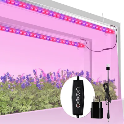 Two LED grow lights illuminating plants with purple and red light, with a controller and power adapter in the foreground.