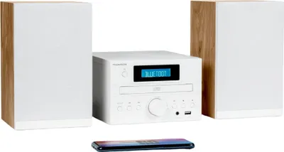 A white and wood-grain home sound system with two speakers and a central unit, placed on a white background. A smartphone is visible in the foreground.