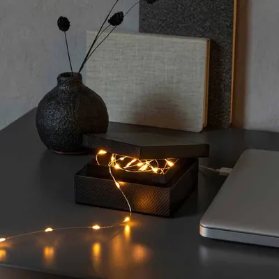 A black box with fairy lights inside, placed on a dark surface next to a vase and books.