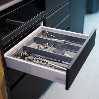 An open kitchen drawer containing a utensil organizer with various kitchen utensils.