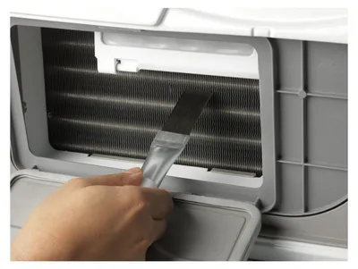 A hand is using a brush to clean the fins of an air conditioner.