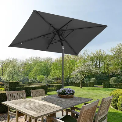 A rectangular patio umbrella shades a wooden table and chairs in a manicured garden.