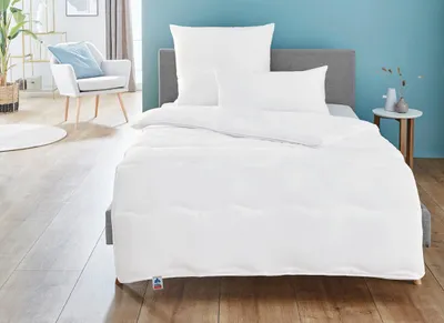 A neatly made bed with white bedding in a room with light wooden floors and a blue wall.