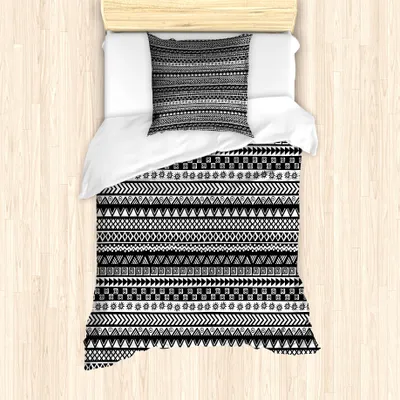 A top-down view of a single bed with a duvet cover and pillow featuring a black and white geometric tribal pattern, placed on a light wooden floor.