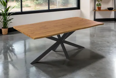 A dining table with a wooden top and a black spider-like base is shown in a room with large windows.